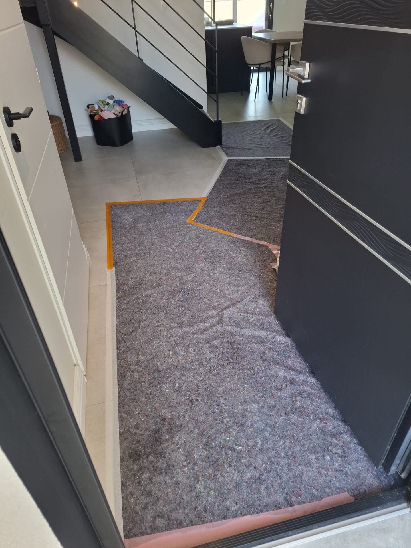 Couloir menant de l’entrée au séjour, recouvert d’un feutre de chantier scotché sur le carrelage avant les travaux